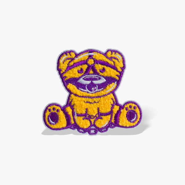 Patch featuring a cute bear in yellow and purple with a playful expression, wearing a BDSM harness and a ball gag. The design is fun and whimsical, combining bold colors with a cheeky style.